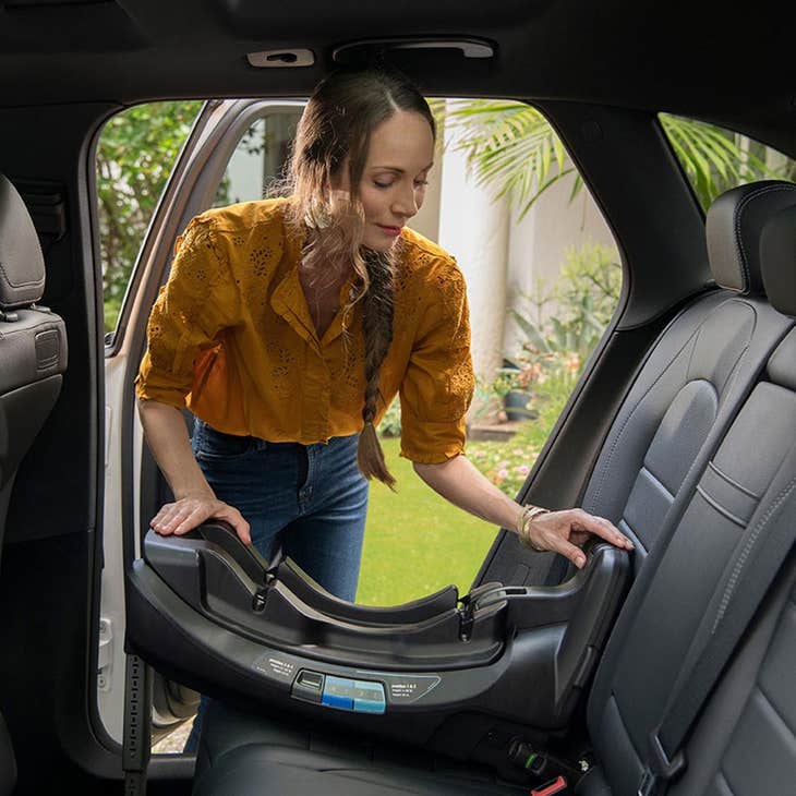 Parenting installing a rear-facing infant car seat base into the backseat of their car.