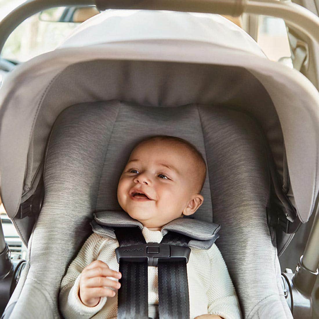 Baby smiling while buckled into a rear-facing infant car seat with canopy up, that is installed in the backseat of a car.